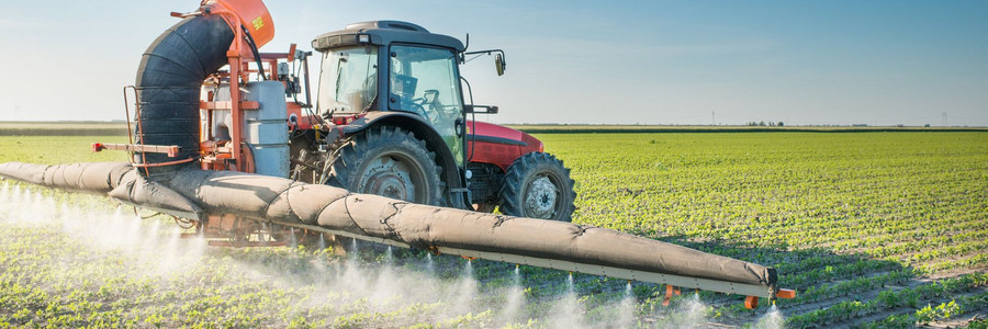 Traktor fährt über Ackerfläche und versprüht Pestizide