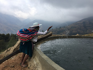 Frau steht an einem Wasserbecken vor dem Hintergrund der Anden und spritzt Wasser in die Luft