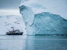 Ein Schiff fährt vor einem Eisberg in der Arktis