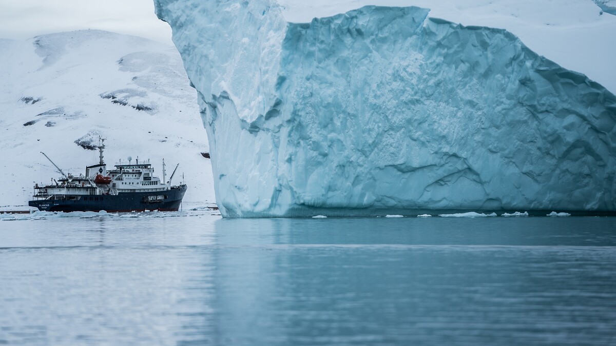 Ein Schiff fährt vor einem Eisberg in der Arktis