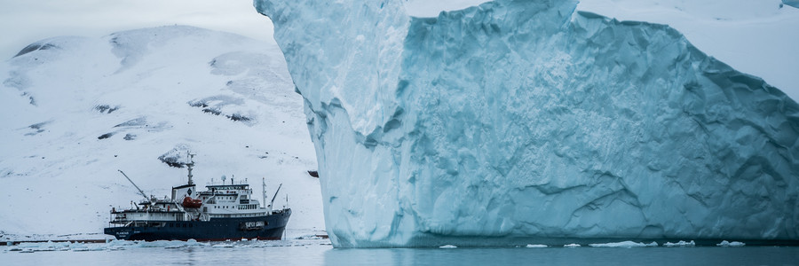 Ein Schiff fährt vor einem Eisberg in der Arktis