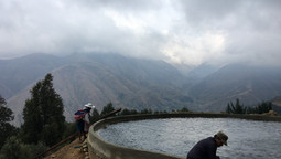 Zwei Personen stehen an einem Wasserbecken vor dem Panorama der Anden