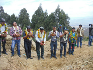 Menschen mit Blumenketten um den Hals weihen ein neu gebautes Wasserbecken in den Anden Boliviens ein