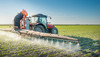 Traktor fährt über Ackerfläche und versprüht Pestizide
