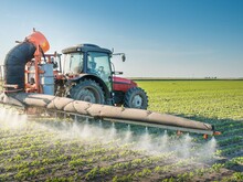 Traktor fährt über Ackerfläche und versprüht Pestizide