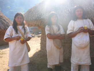 Drei Junge Kogi Männer stehen vor runden Lehmhütten in der Sierra Nevada de Santa Marta in Kolumbien